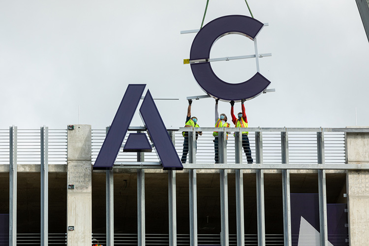 A large letter A and C being installed on the East facing side of the Highland Campus parking garage.