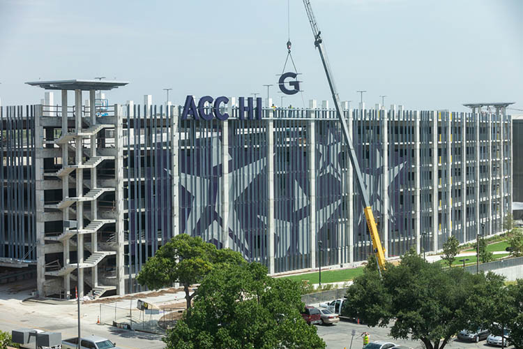 A crane lowers a large letter G next to the letters that will spell, ACC HIGHLAND, onto the East facing side of the Highland Campus parking garage.