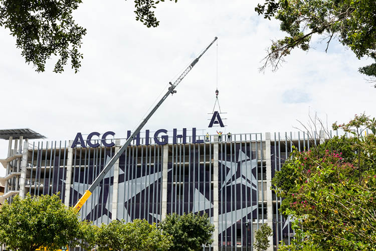 A crane lowers a large letter A next to the letters that will spell, ACC HIGHLAND, onto the East facing side of the Highland Campus parking garage.